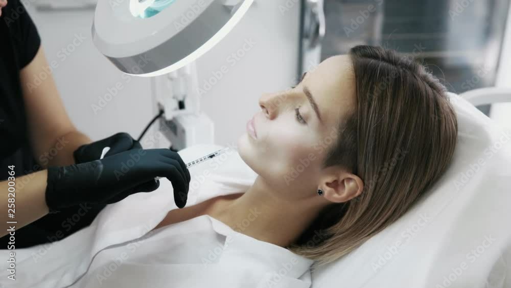Close up cosmetologist with syringe makes woman injections and looks through cosmetic magnifier Close up cosmetologist with syringe makes woman injections and looks through cosmetic magnifier