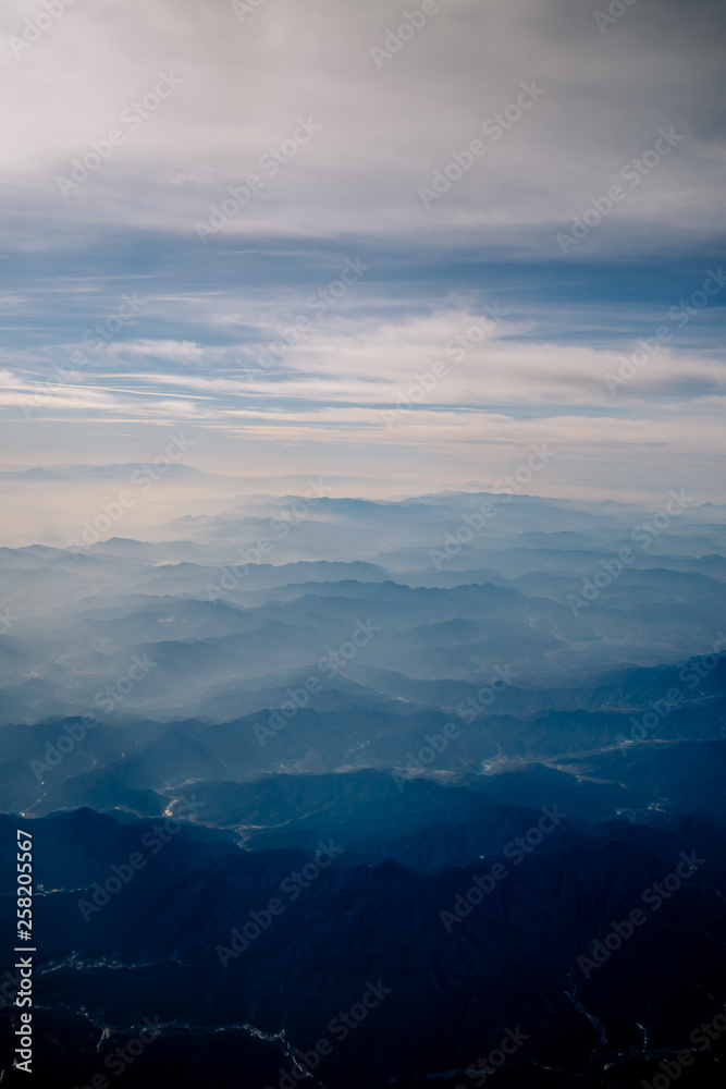 An aerial view of Chinese mountains from the airplane flying high above the ground. A look from the plane window.