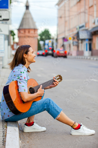 Girl in a blue shirt and jeans with a guitar in the old town