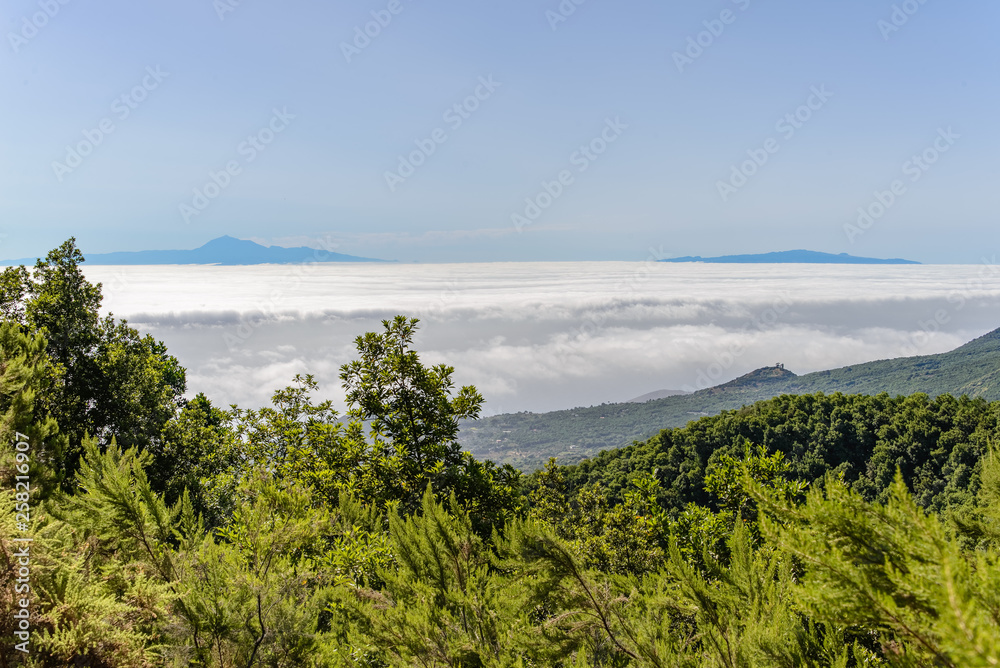 A landscape looking over a sea of clouds to two distant islands. They are Tenerife and La Gomera, seen from La Palma.