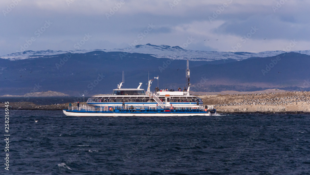 Big tourist white ship on a tour excursion to the islands in Beagle Channel, on dark blue waters with cloudy mountains on the background on a sunny day. Ushuaia, Tierra del Fuego, Argentina