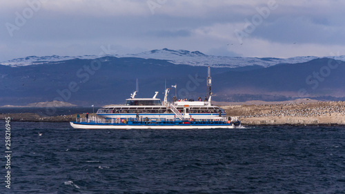 Big tourist white ship on a tour excursion to the islands in Beagle Channel, on dark blue waters with cloudy mountains on the background on a sunny day. Ushuaia, Tierra del Fuego, Argentina © AgusCami