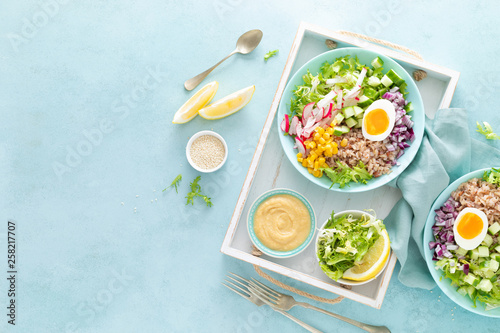 Buddha bowl with boiled egg, rice and vegetable salad of fresh lettuce, radish, cucumber, corn, onion and sesame seeds and chickpea sauce