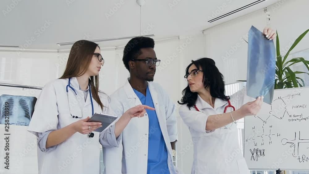 Three multi national doctors discussing xray of lungs of the patient during work day.