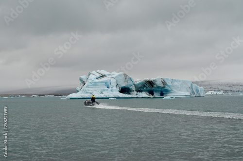 Man in motor boat  zodiac  cruising across Iceland Glacier Lagoon with Iceberg in background