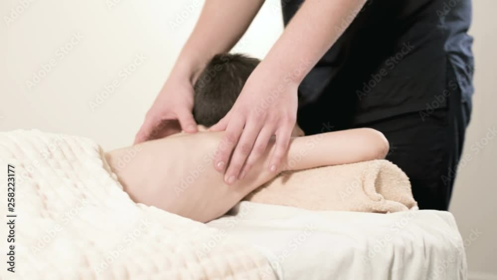 A male physiotherapist masseur makes a healing relaxing massage to a little smiling boy lying on a massage bed. Massage of the loin and back A male physiotherapist masseur makes a healing relaxing massage to a little smiling boy lying on a massage bed. Massage of the loin and back