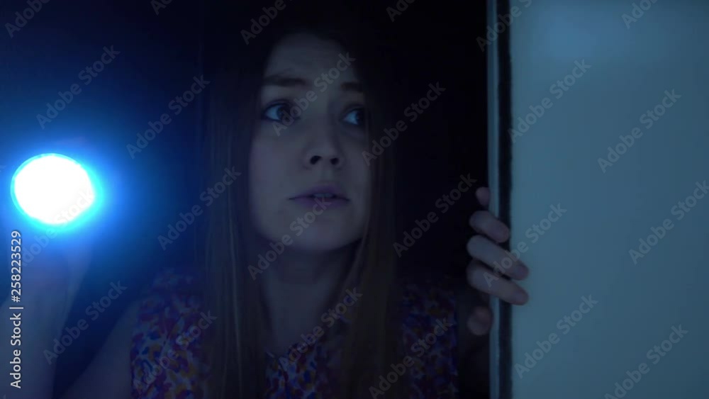 Attractive blond-haired woman holding flashlight and opening a door, checking a room in the darkness. Nightmare of young woman that feels fear and scare. Somebody attacked girl. Violence concept.