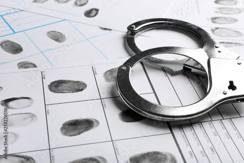 Handcuffs and fingerprint record sheets, closeup. Criminal investigation photo