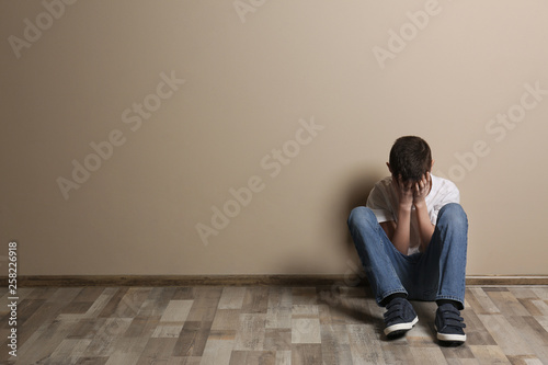 Upset boy sitting on floor at color wall. Space for text