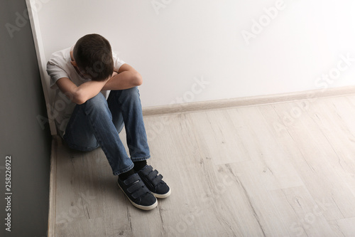 Upset boy sitting on floor indoors. Space for text