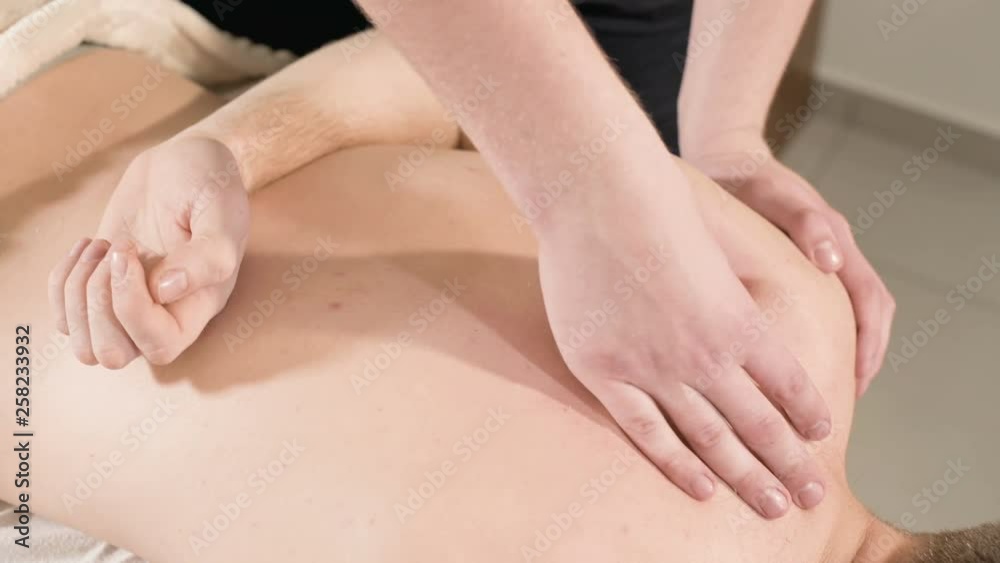 Close-up Young male physiotherapist masseur doing therapeutic massage with hand stretching and shoulder blades for men in the massage room Close-up Young male physiotherapist masseur doing therapeutic massage with hand stretching and shoulder blades for men in the massage room