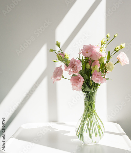 Close up of pink lisianthus  flowers in glass vase on white table with bright sunlight and hard shadows from window