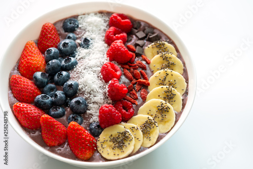 Acai Berry superfoods smoothies white bowl with chia seeds, strawberry, goji berry, coconut, blueberry, raspberry toppings, and chocolate chip on white background