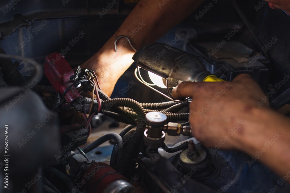 Young man mechanic repairing car in garage shop,car service, repair, maintenance and people concept - auto mechanic man with lamp working at car service center.
