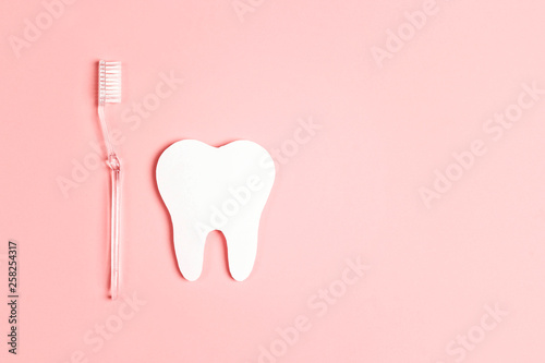 White paper tooth with toothbrush on pink background. Dental health concept. Flat lay, top view, copy space.