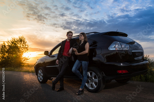 Couple standing near the car in a summer evening