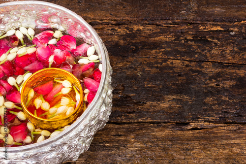 Water with rose petals and jasmine in silver and golden bowl on wet old wood background for Songkran festival in thailand