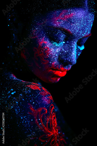 Profile portrait of a beautiful girl alien. Ultraviolet body art blue night sky with stars and pink jellyfish