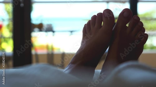 Wallpaper Mural Woman lying in hotel on a bed. Close up of waving feet against tropical sea view. 3840x2160 Torontodigital.ca