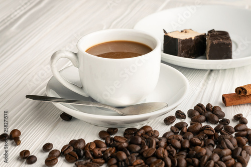 A cup of coffee with milk and coffee beans scattered on the table and souffle candy in chocolate