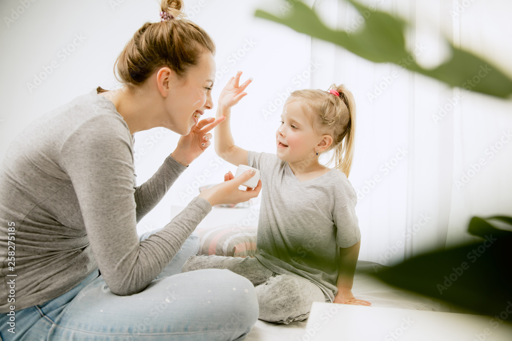 Young mother and her little daughter at home at sunny morning. Soft pastel colors. Happy family time on weekend. Mother's Day concept. Family, love, lifestyle, motherhood and tender moments concepts. Young mother and her little daughter at home at sunny morning. Soft pastel colors. Happy family time on weekend. Mother's Day concept. Family, love, lifestyle, motherhood and tender moments concepts.