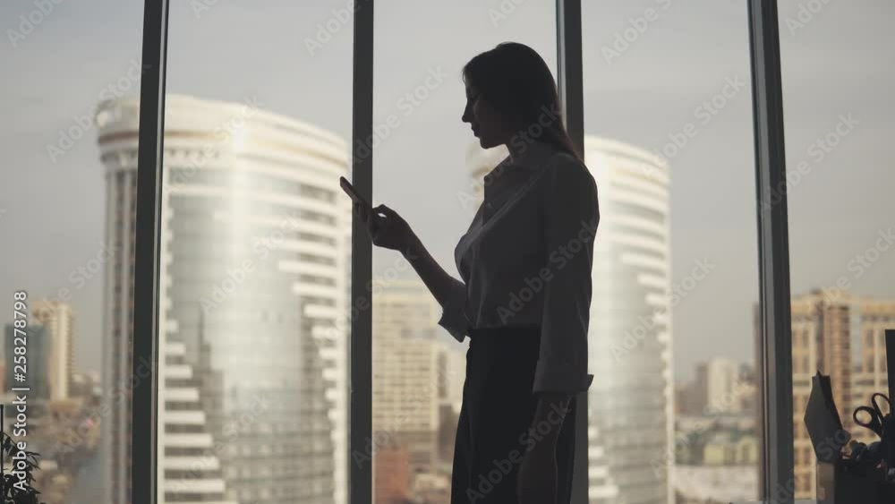Businesswoman silhouette with a mobile phone in hand. girl uses a smartphone in the office Businesswoman silhouette with a mobile phone in hand. girl uses a smartphone in the office