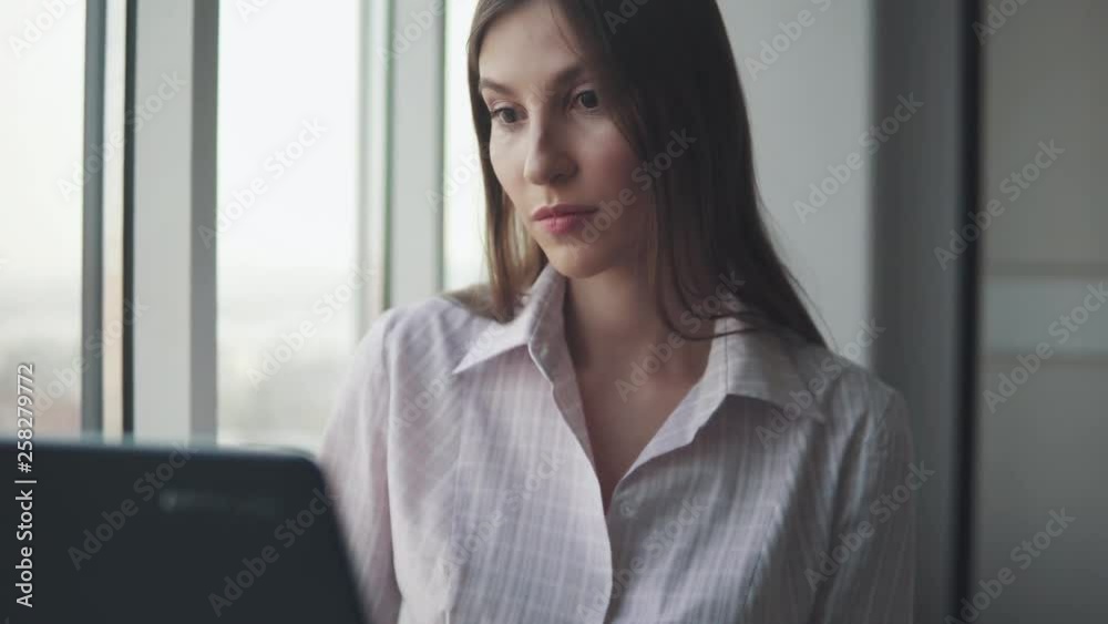 Portrait of business woman working on a laptop by the window in the office. Portrait of business woman working on a laptop by the window in the office.