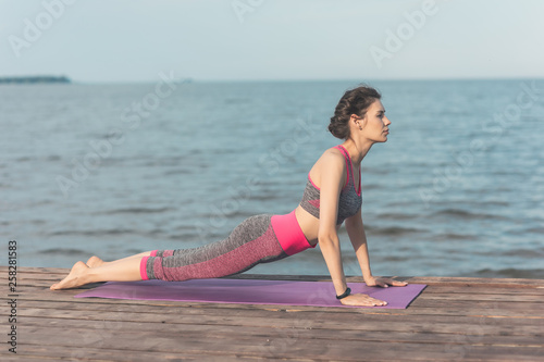 Sporty young girl in the morning on the pier on seashore, practicing yoga. Woman do gymnastics outdoors. Health and Yoga Concept. Female meditation for fitness lifestyle the nature background