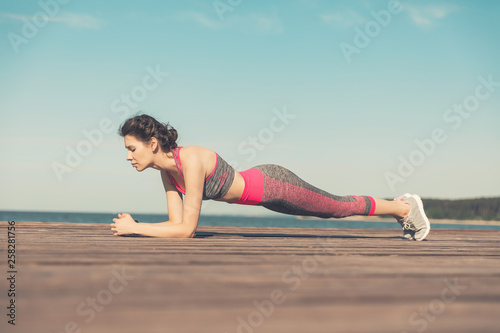 Sporty young girl in the morning on the pier on seashore, practicing yoga. Woman do gymnastics outdoors. Health and Yoga Concept. Female meditation for fitness lifestyle the nature background