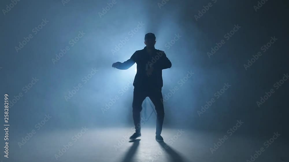 A dark silhouette of a singer on the stage, dancing alone during performance on dark blue neon background with smoke and lights, slow motion. A dark silhouette of a singer on the stage, dancing alone during performance on dark blue neon background with smoke and lights, slow motion.
