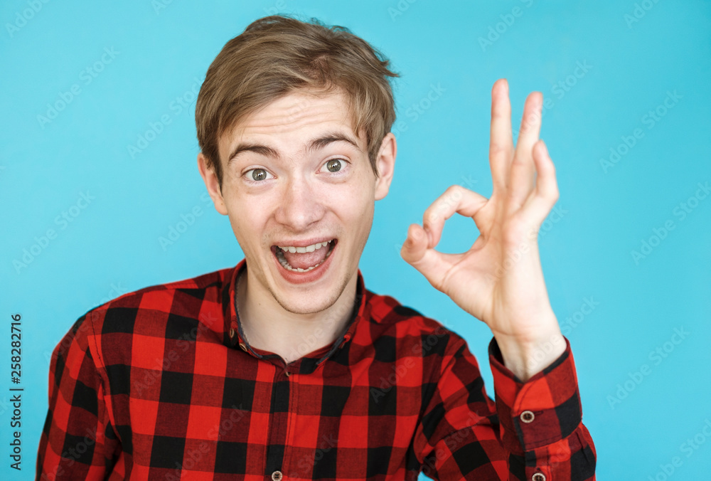 young male satisfied teenager in red shirt on blue background young male satisfied teenager in red shirt on blue background