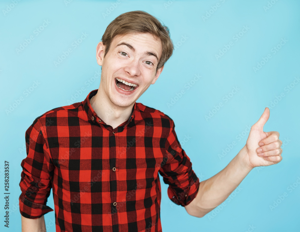 young male teenager in red shirt on blue background shows class