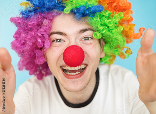 young funny male teenager in white t-shirt on blue background in clown wig close-up portrairt photo