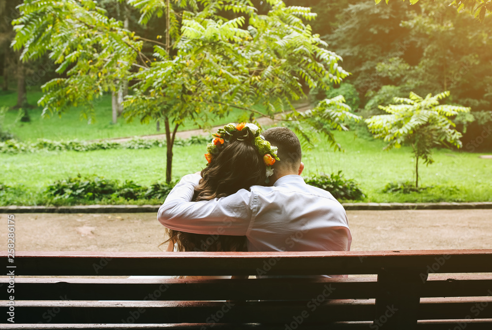 Fototapeta premium Wedding couple in love is sitting on the bench in the park. Bride and groom are hugging. Romantic concept.Warm summer day outdoors.