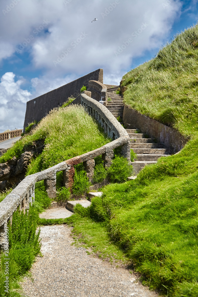 Biarritz, France. Atlantic ocean coast. Old stone stairs on slope of green hill. Sunny summer day