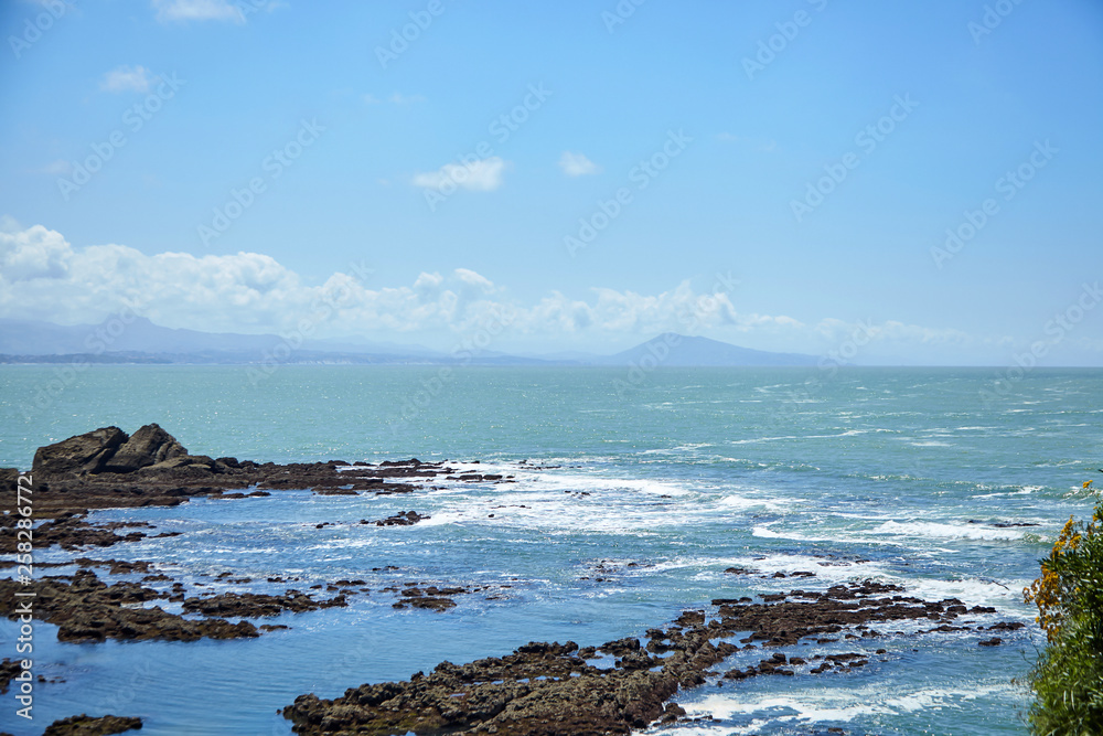 Seascape. Waves with white foam, sharp stones and blue sky with clouds. Rocky Atlantic ocean coast