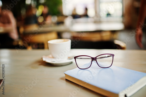 Close up photo of notebook with glasses against cup of coffe at cafe table. Eyewear concept.
