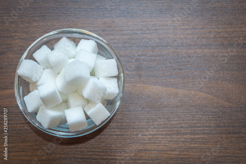Top view of sugar cubes in a glass bowl on a wooden background. Copy space provided.