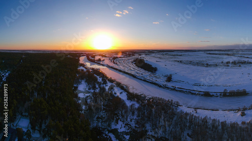 The forest and the frozen river with the appearance of thawed patches in the spring at sunset, when there is still snow in Russia from the height