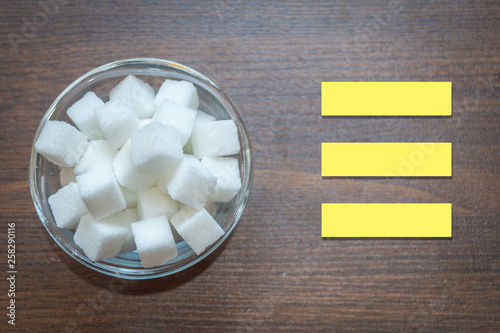 Top view of sugar cubes in a glass bowl on a wooden background. Copy space provided. Text space for writing disadvantages of sugar. Diabetes caused by sugar,