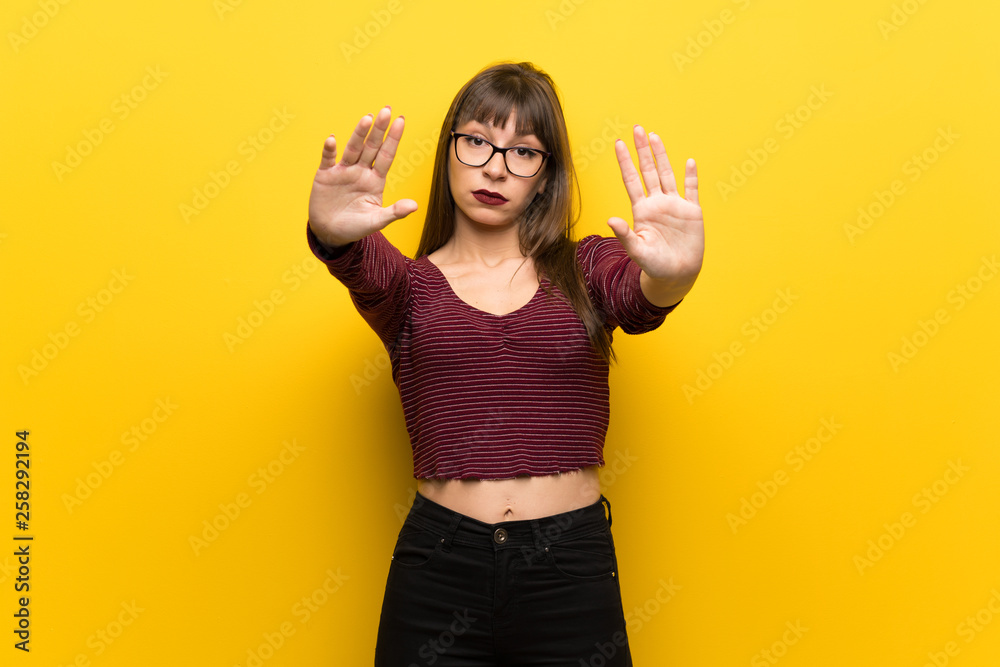 Obraz premium Woman with glasses over yellow wall making stop gesture and disappointed