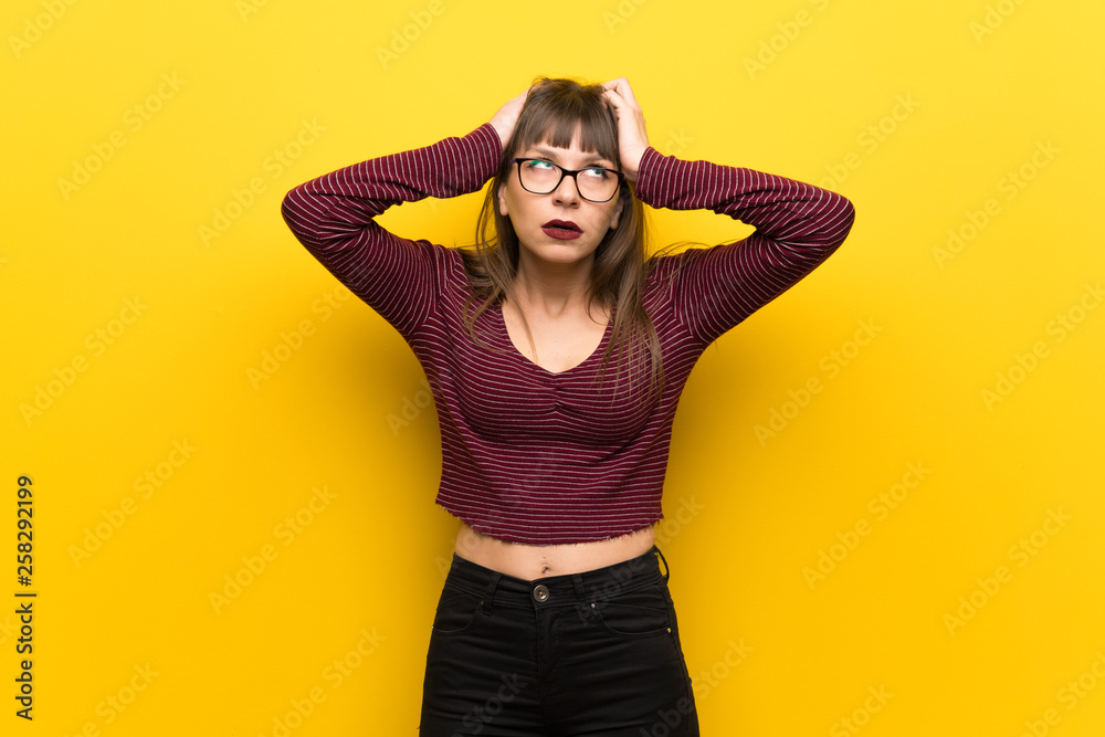 Woman with glasses over yellow wall frustrated by a bad situation Woman with glasses over yellow wall frustrated by a bad situation