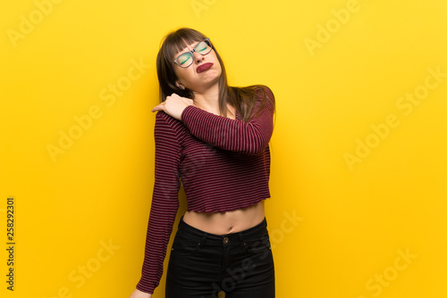Woman with glasses over yellow wall suffering from pain in shoulder for having made an effort