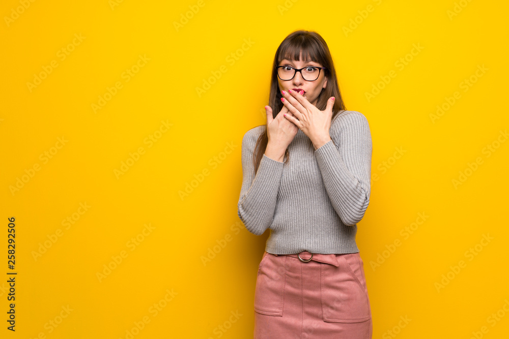 Woman with glasses over yellow wall covering mouth with hands for saying something inappropriate Woman with glasses over yellow wall covering mouth with hands for saying something inappropriate