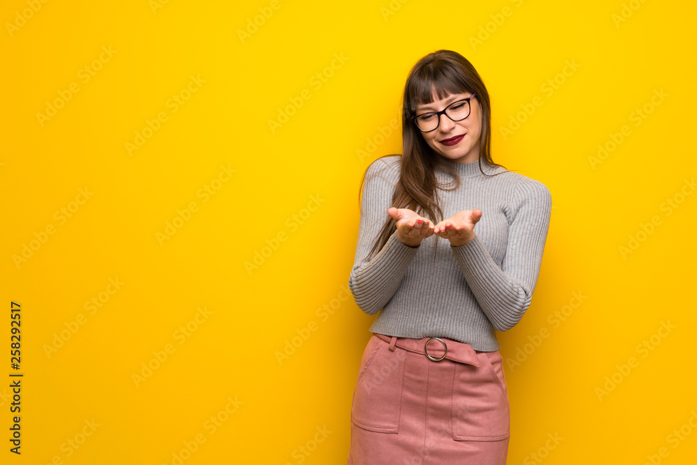 Woman with glasses over yellow wall holding copyspace imaginary on the palm to insert an ad Woman with glasses over yellow wall holding copyspace imaginary on the palm to insert an ad