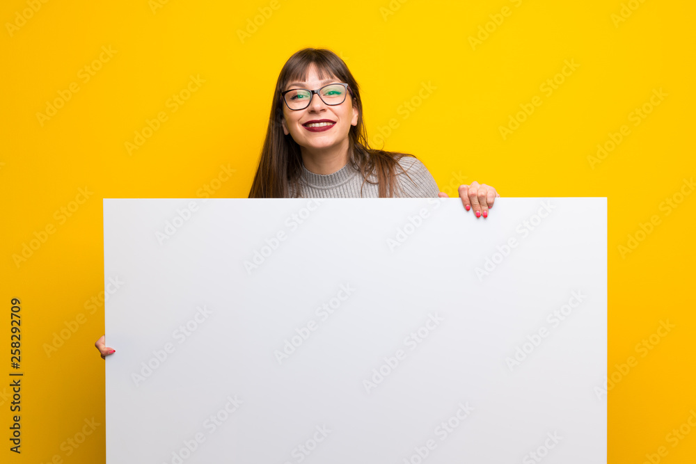 Woman with glasses over yellow wall holding an empty white placard Woman with glasses over yellow wall holding an empty white placard