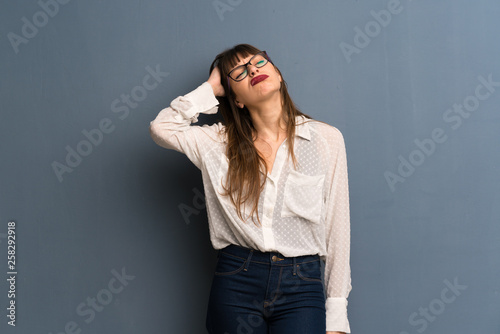 Woman with glasses over blue wall with an expression of frustration and not understanding