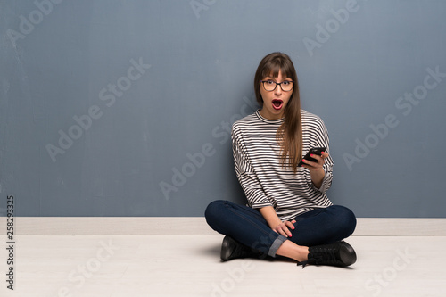 Woman with glasses sitting on the floor surprised and sending a message © luismolinero