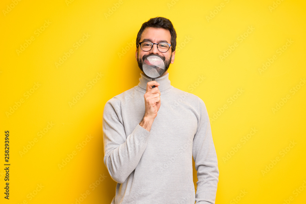 Man with beard and turtleneck taking a magnifying glass and showing teeth through it Man with beard and turtleneck taking a magnifying glass and showing teeth through it