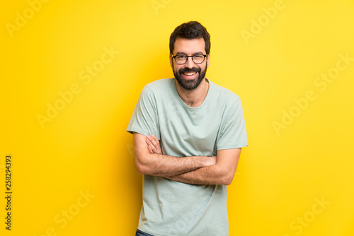 Man with beard and green shirt keeping the arms crossed while smiling